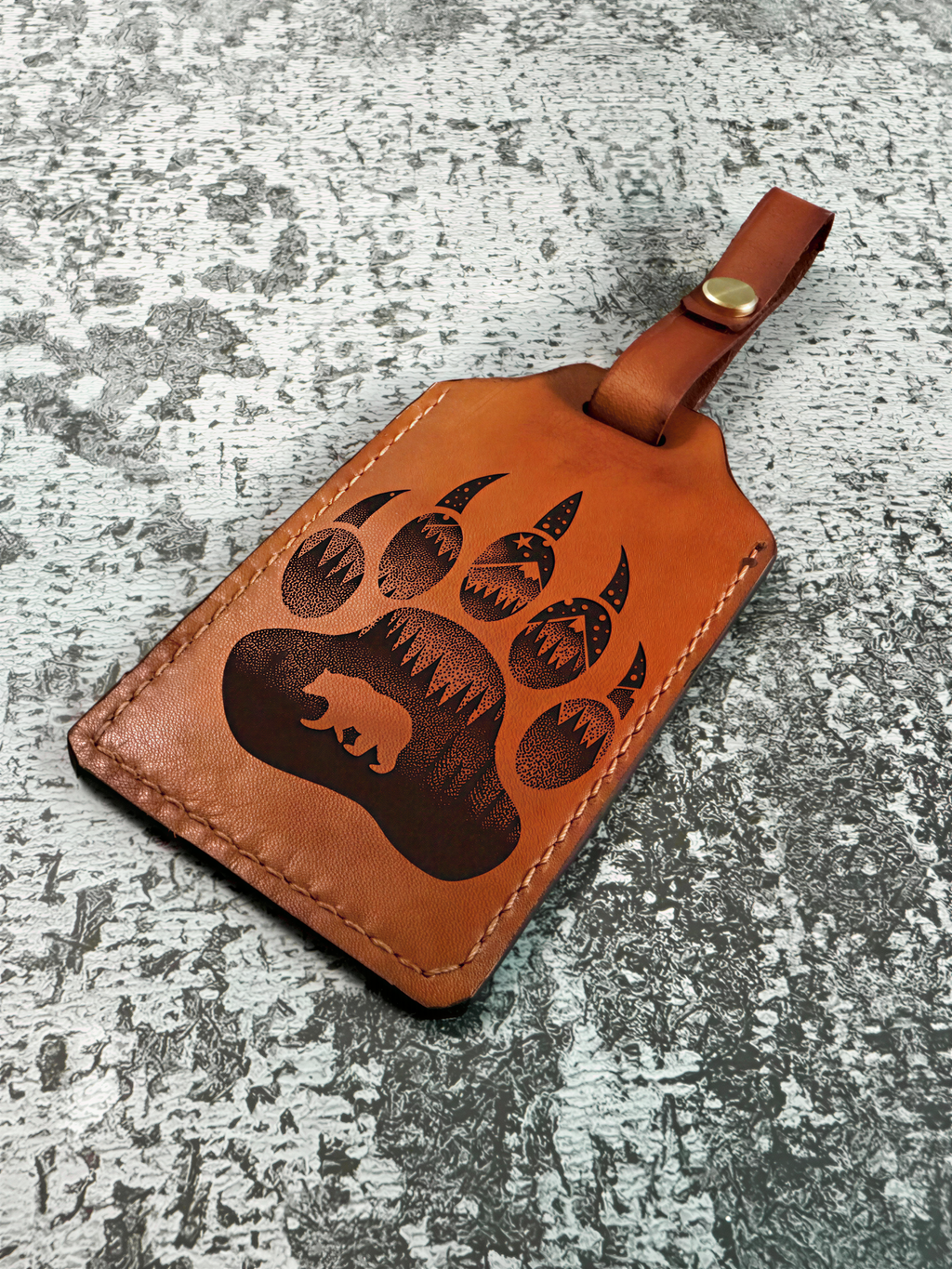 A brown leather luggage tag with a bear paw print design printed on it.